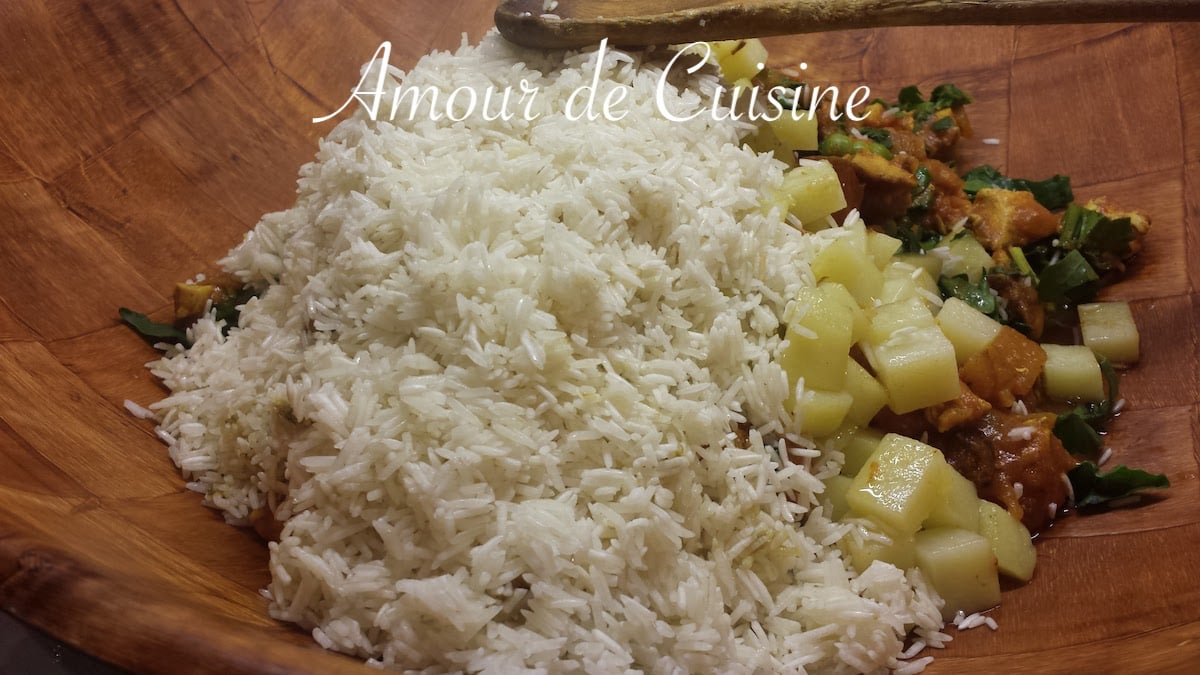 Terrine en bois contenant du riz basmati rincé, des cubes de pommes de terre, et une préparation de légumes et poulet en sauce pour la recette du riz djerbien