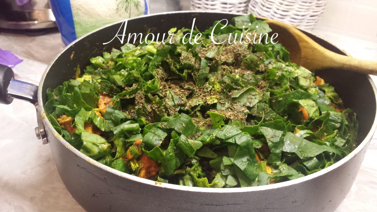 Poêle remplie d’épinards frais hachés ajoutés à une préparation de poulet, tomates et légumes en cours de cuisson pour un riz djerbien tunisien traditionnel