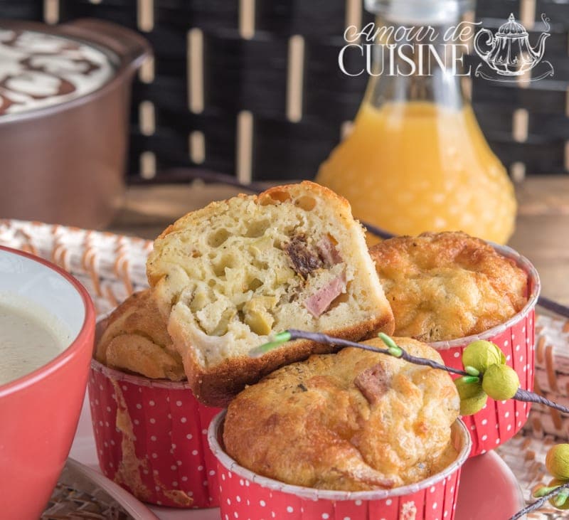 Muffins salés à la mortadelle, olives et tomates séchées, présentés dans des caissettes rouges à pois blancs, accompagnés d’un verre de jus d’orange et d’un bol de velouté crémeux
