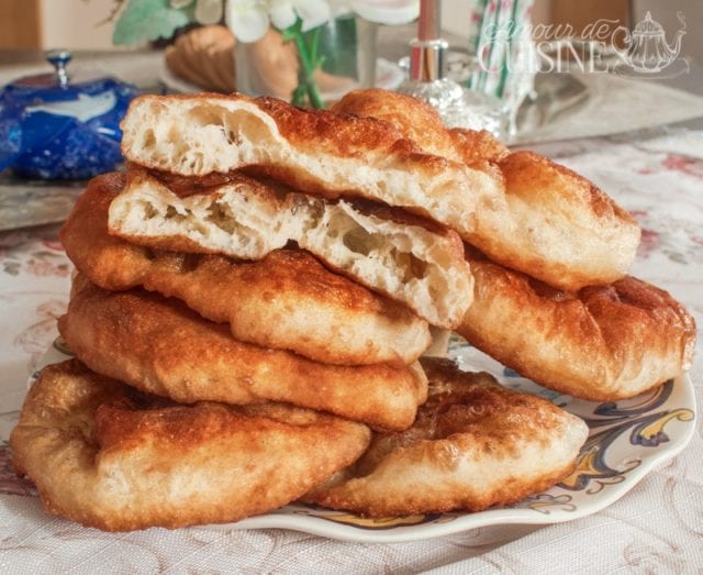 Sfenj maison empilés sur une assiette, avec un beignet ouvert pour montrer la mie légère, aérée et moelleuse à l’intérieur.
