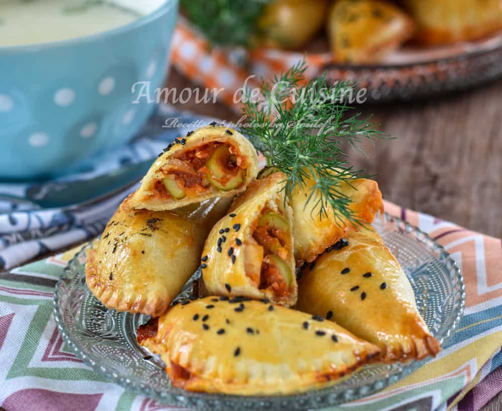 Assiette de chaussons empanadas au poulet, dorés au four, garnis d’olives vertes et d’une farce à la tomate, parsemés de graines de nigelle, accompagnés d’aneth frais et d’un bol de soupe crémeuse en arrière-plan