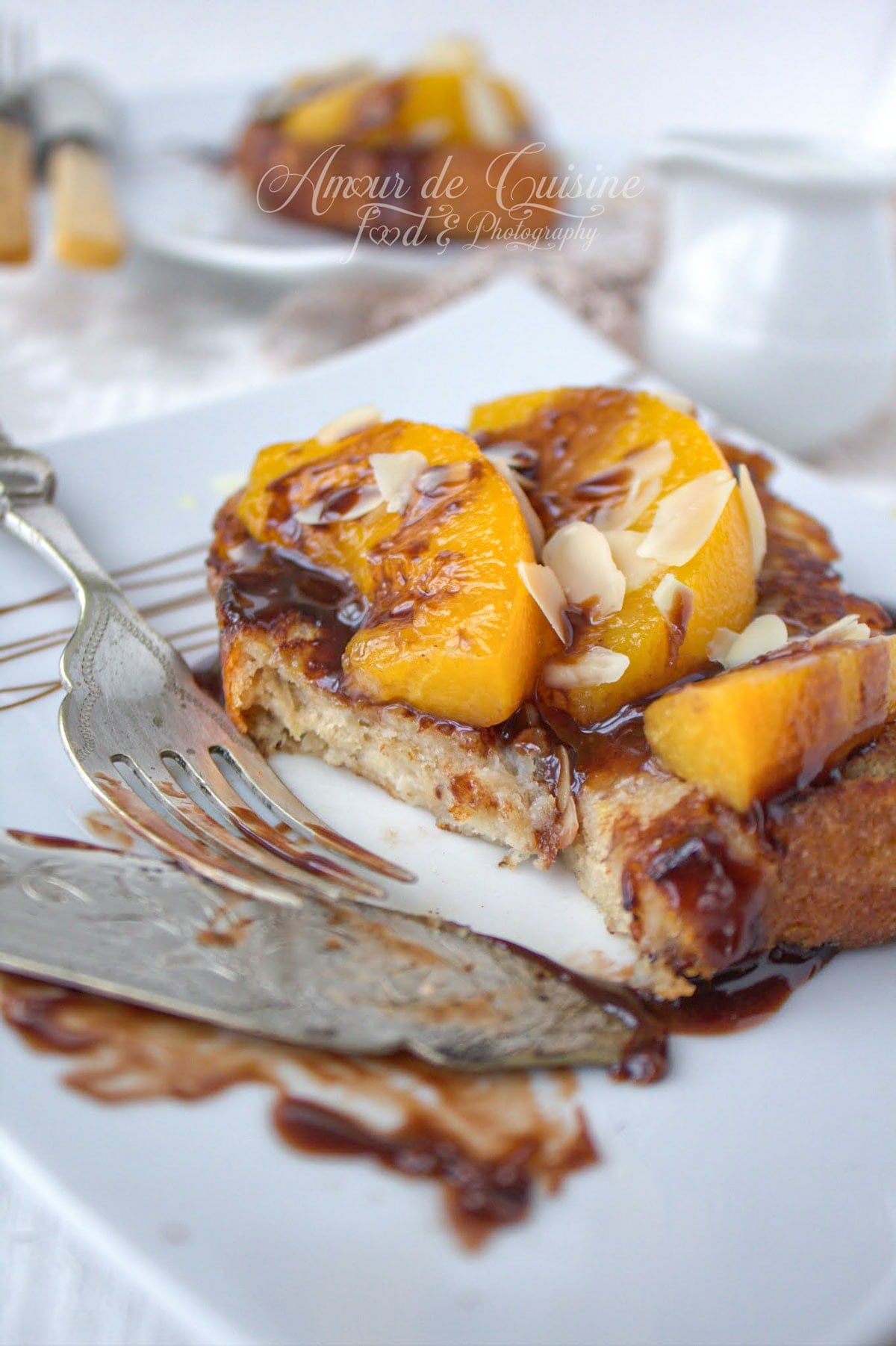 Part de brioche perdue moelleuse aux pêches caramélisées, nappée de sauce au chocolat et parsemée d’amandes effilées.