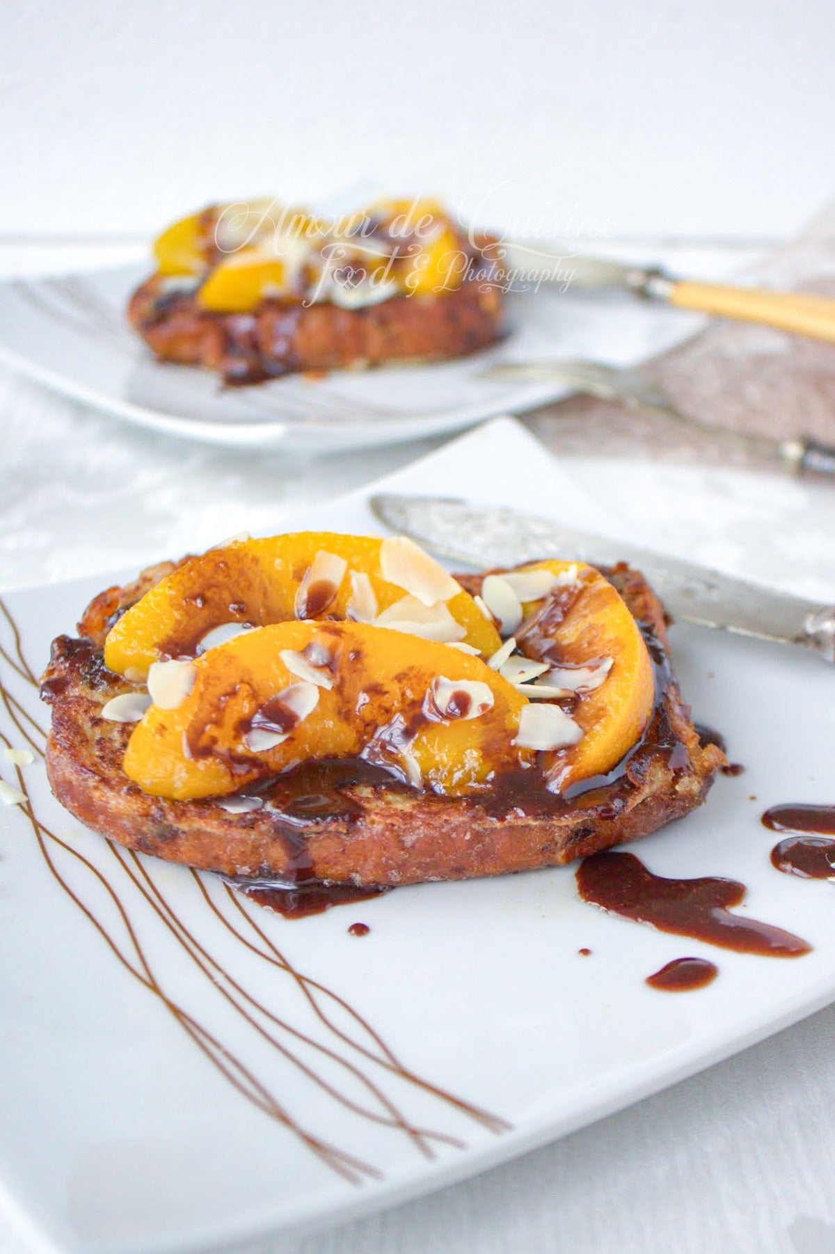 Brioche perdue moelleuse garnie de pêches caramélisées, sauce au chocolat et amandes effilées, servie sur une assiette blanche.