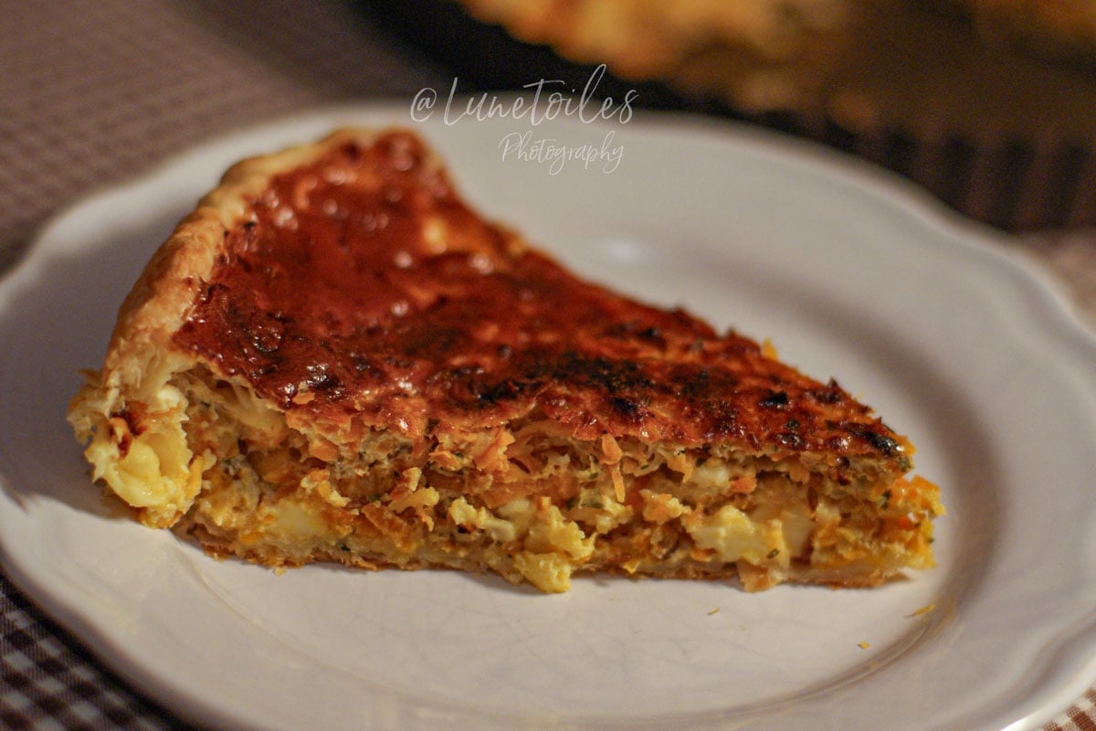 Part de quiche aux carottes au gouda et cumin servie dans une assiette, avec texture fondante et pâte dorée.