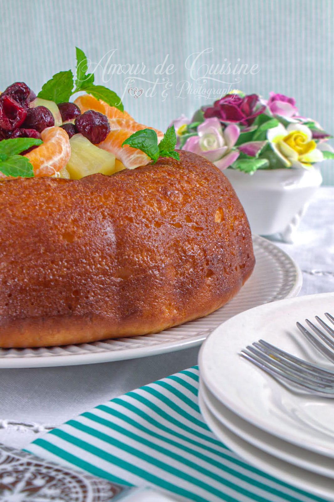 Savarin à l’orange sans rhum présenté entier sur un plat, garni de quartiers de mandarine, ananas, cerises et feuilles de menthe.