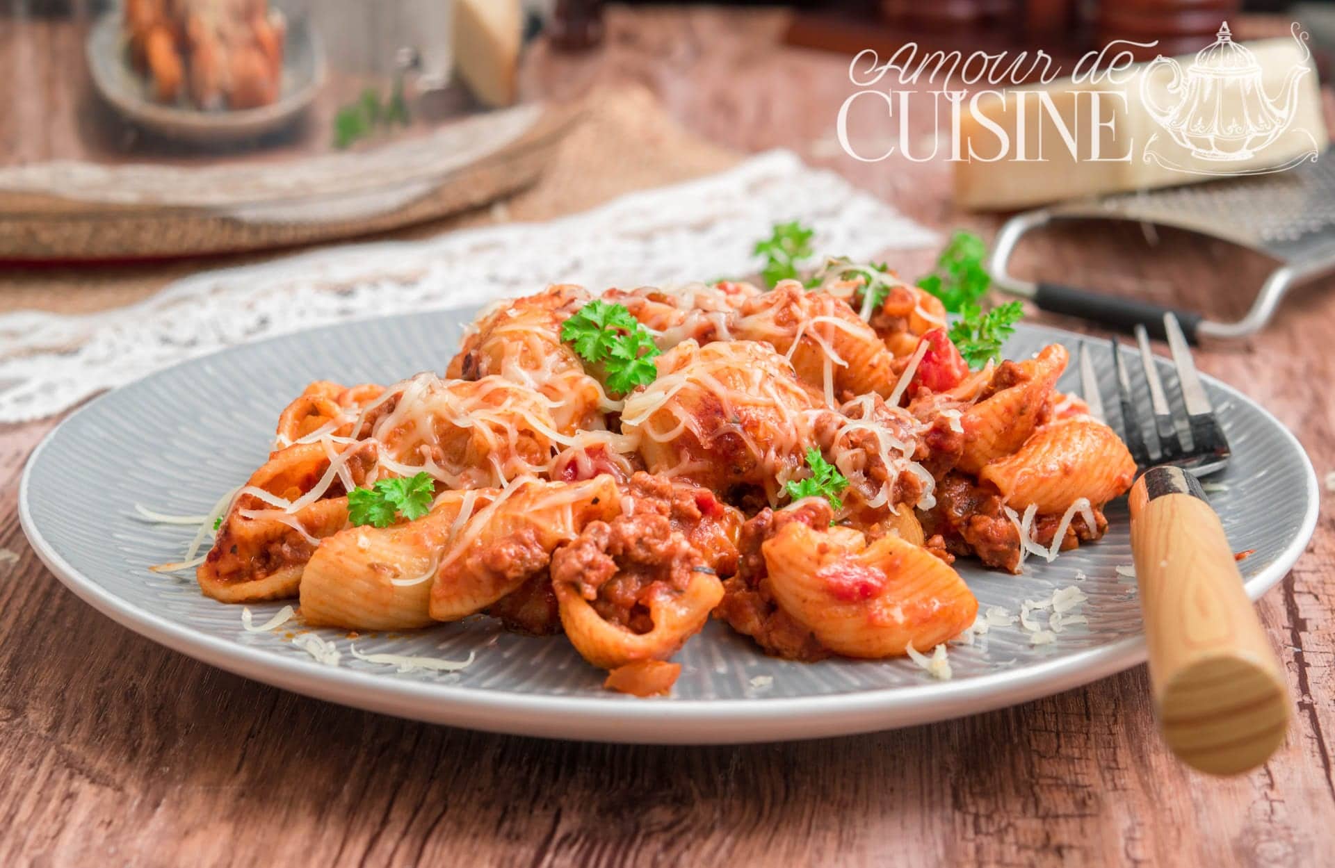 Plate of penne rigate in tomato sauce with ground beef, topped with melted grated cheese and fresh parsley, served on a grey plate with a wooden-handled fork placed beside it