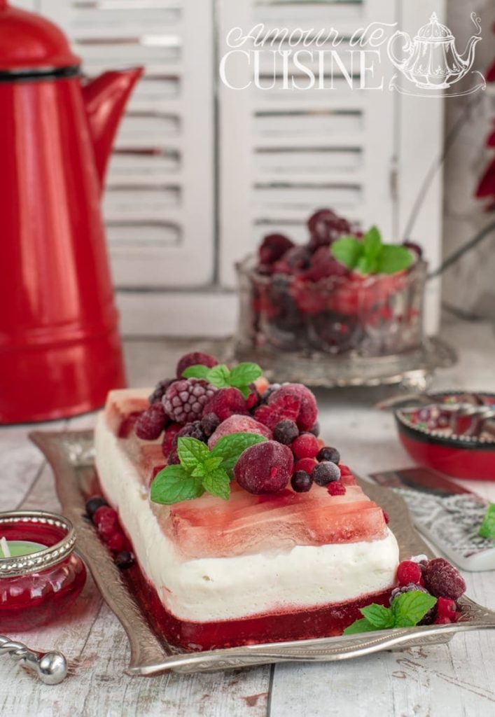 Layered summer berry panna cotta terrine with vanilla cream and red fruit jelly, topped with frozen mixed berries and mint leaves, served on a vintage silver tray