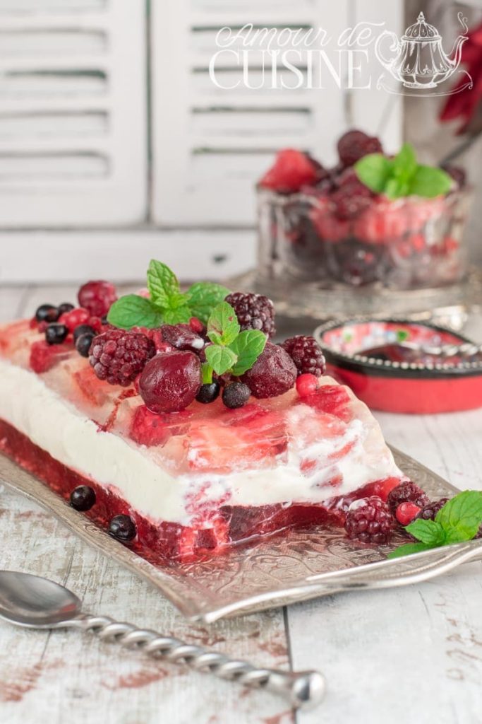 Slice of summer berry panna cotta terrine with vanilla layer and double fruit jelly, topped with frozen berries and fresh mint, served on an ornate silver platter with vintage decor