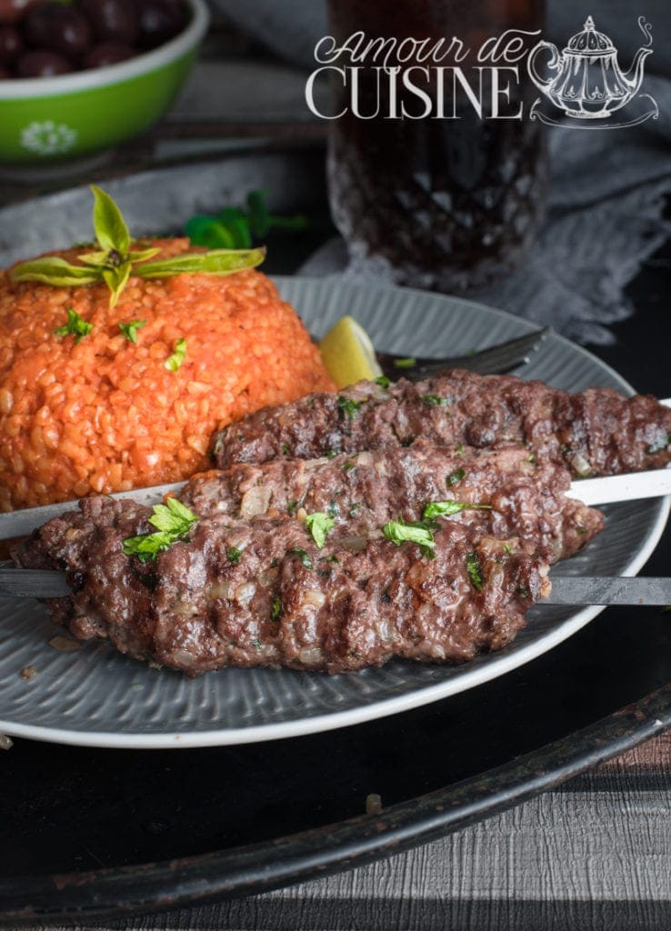 Grilled beef kafta kabob skewers served with tomato bulgur pilaf, garnished with fresh herbs on a grey plate