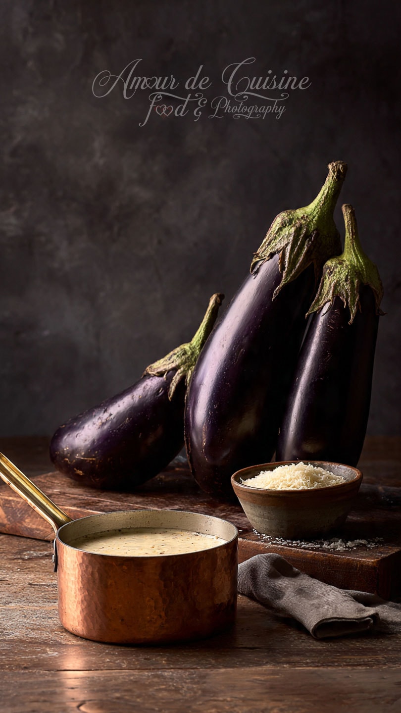 Aubergines fraîches posées sur une planche en bois, accompagnées d’un bol de fromage râpé et d’une casserole de sauce crémeuse prête à l’emploi