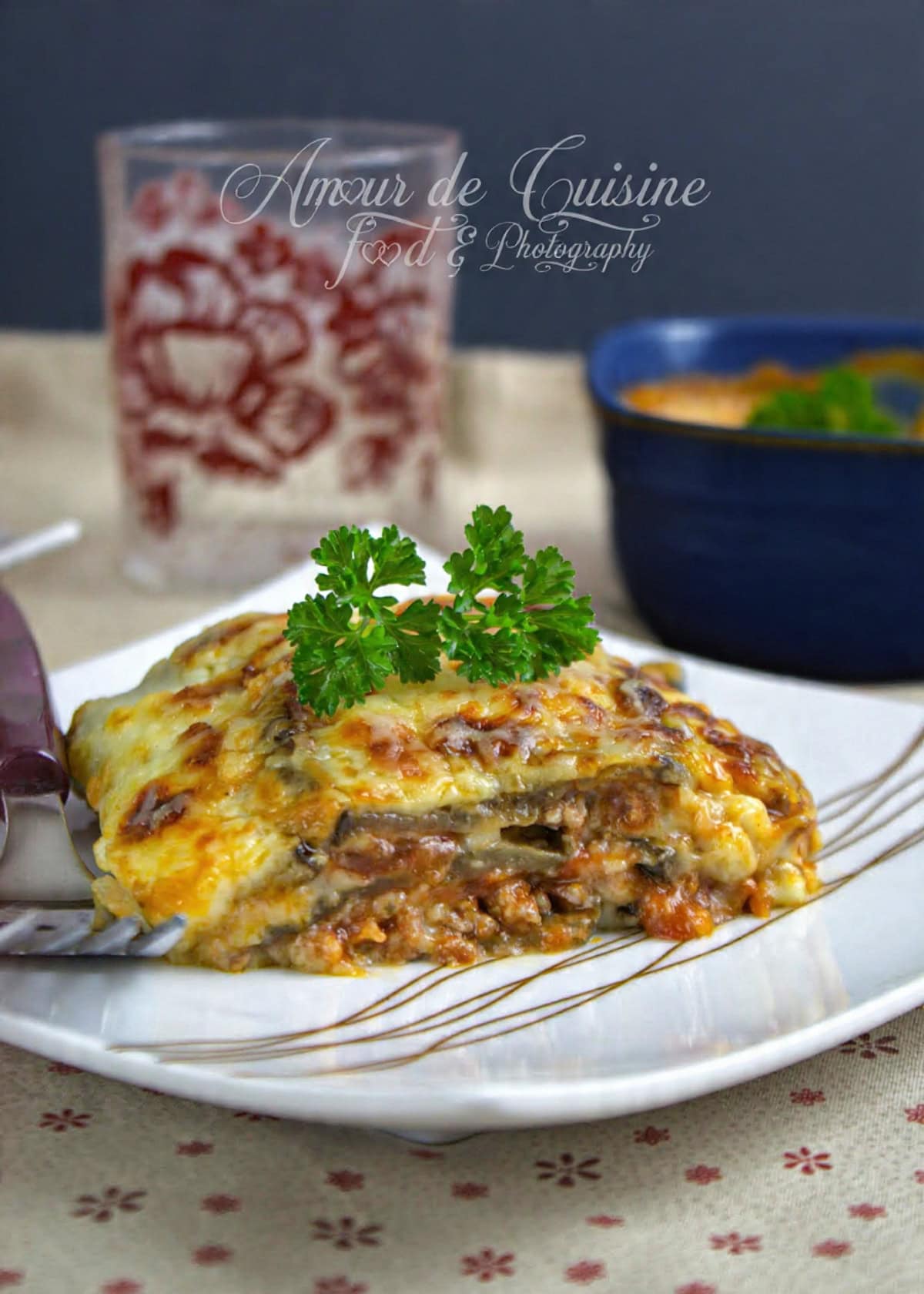Part de lasagnes aux aubergines garnie de sauce bolognaise et béchamel, gratinée au fromage et servie sur une assiette, décorée d’un brin de persil