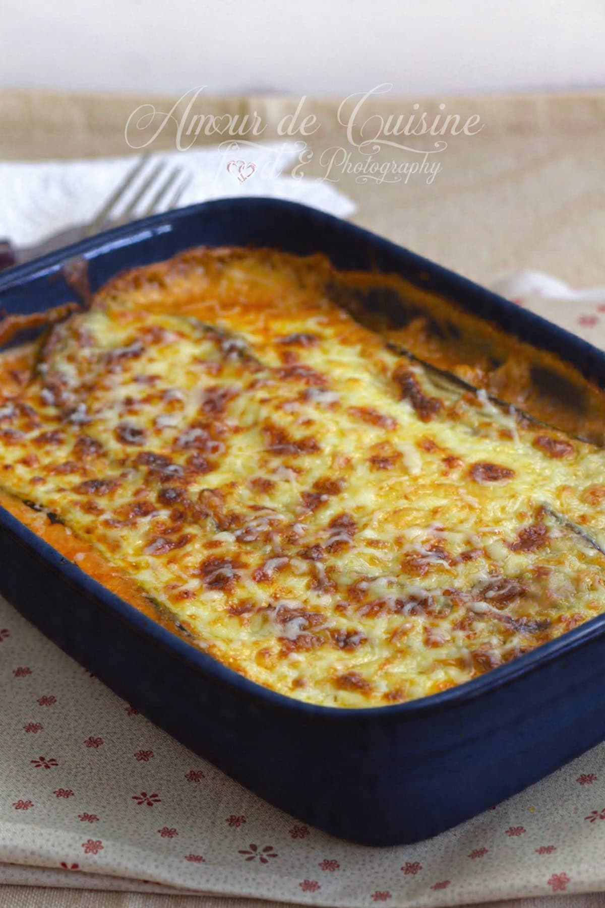 Plat de lasagnes aux aubergines fraîchement sorties du four, avec un gratiné doré et fondant dans un moule rectangulaire bleu.