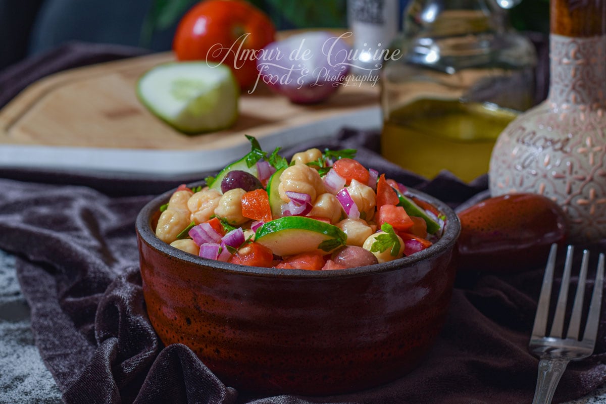 Salade de pois chiche fraîche avec concombre, tomates, oignon rouge, persil et olives, servie dans un bol rustique.
