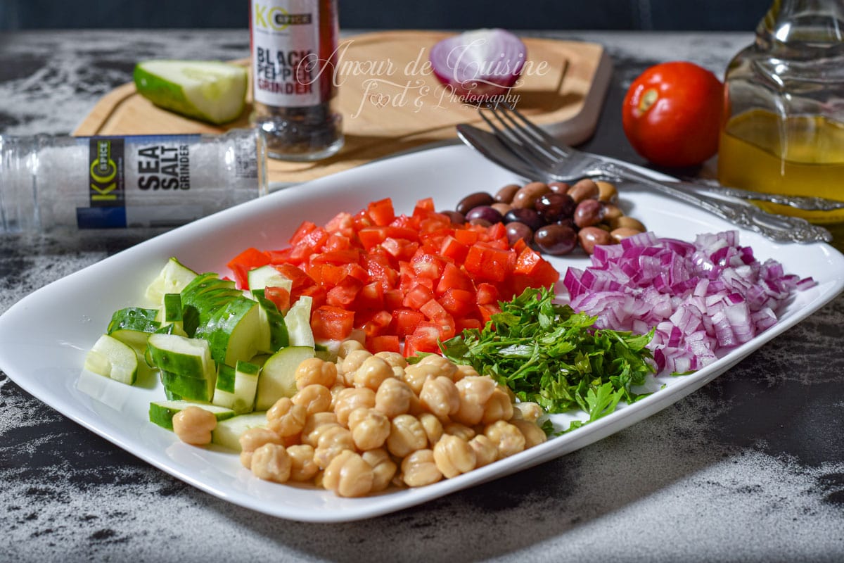 Ingrédients pour salade de pois chiche avec concombre, tomates, oignon rouge, persil, olives, huile d’olive, sel et poivre.