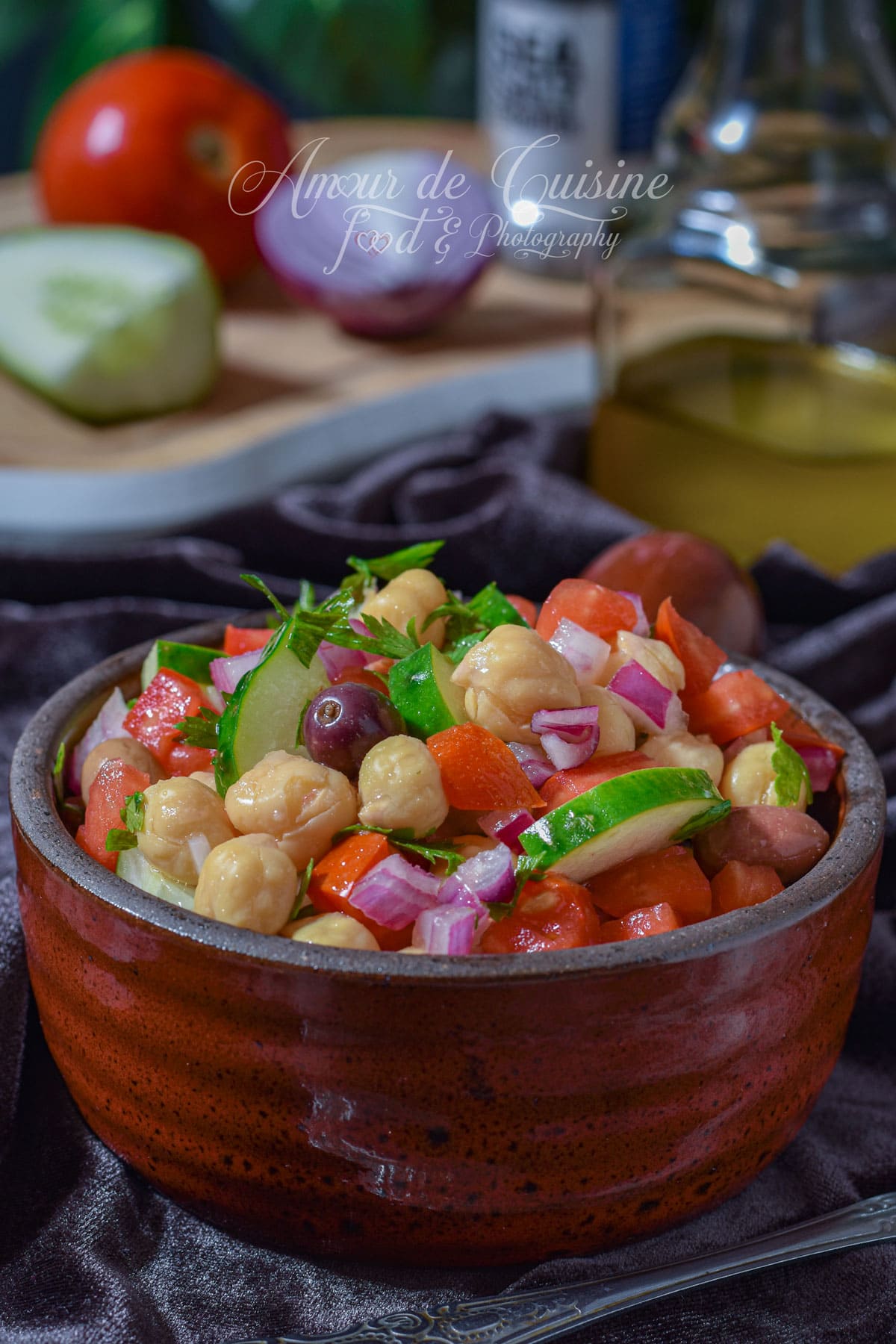Salade de pois chiche facile avec tomates, concombre, oignon rouge, persil et olives violettes dans un bol en terre cuite.