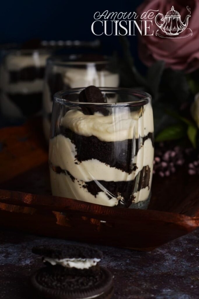 Individual Oreo tiramisu served in a clear glass, showing elegant layers of crushed Oreo cookies and creamy mascarpone filling, topped with an Oreo cookie, set on a wooden tray with cookies in the foreground.