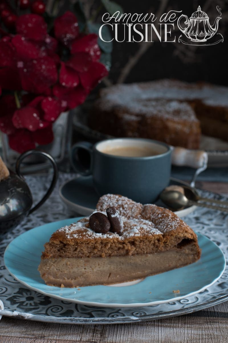 Part de gâteau magique au café à trois couches servie sur une assiette bleue, accompagnée d'une tasse de café, décorée de grains de café en chocolat et saupoudrée de sucre glace.