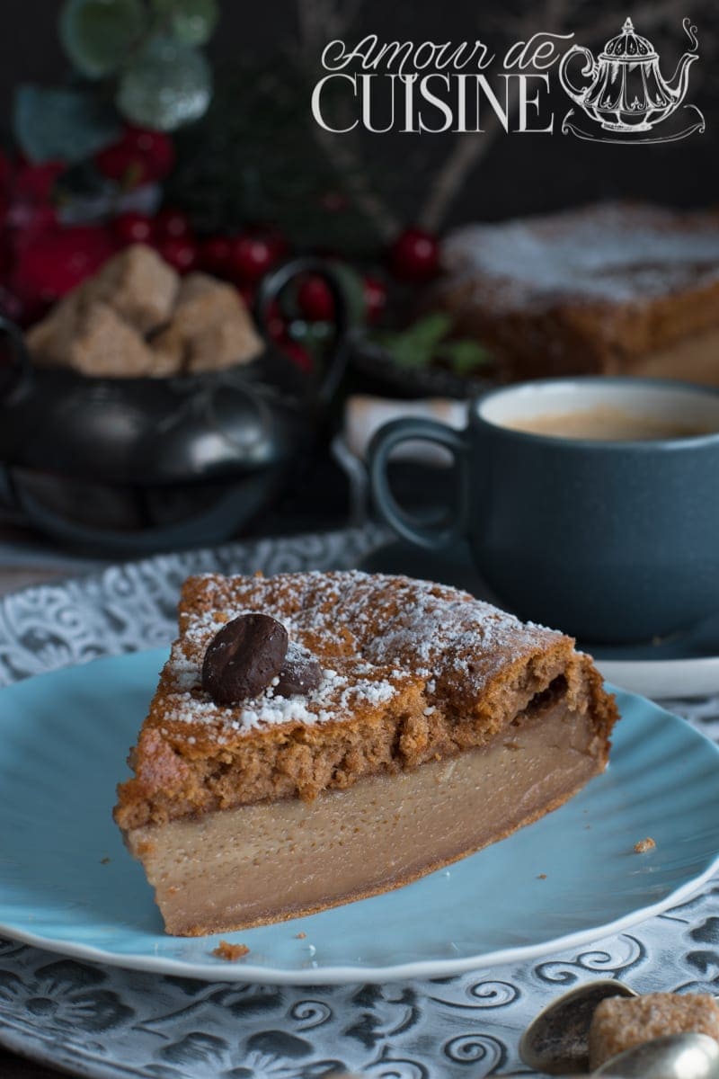 Part de gâteau magique au café sur assiette bleue, montrant ses trois couches distinctes, décorée de grains de café en chocolat et saupoudrée de sucre glace, avec une tasse de café et des morceaux de sucre en arrière-plan