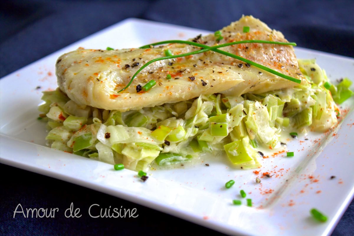Dos de cabillaud poêlé sur fondue de poireaux crémeuse, servi dans une assiette blanche avec ciboulette et poivre