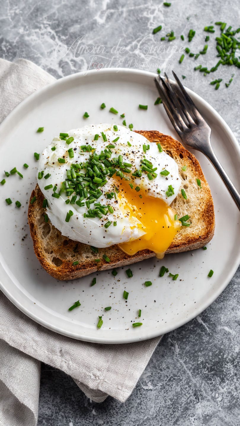 Oeuf poché au jaune coulant servi sur une tranche de pain grillé, parsemé de ciboulette et de poivre noir pour un brunch facile et gourmand