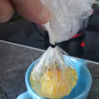 Préparation d’un oeuf poché en bourse de film alimentaire, assaisonné puis refermé avant cuisson dans l’eau chaude