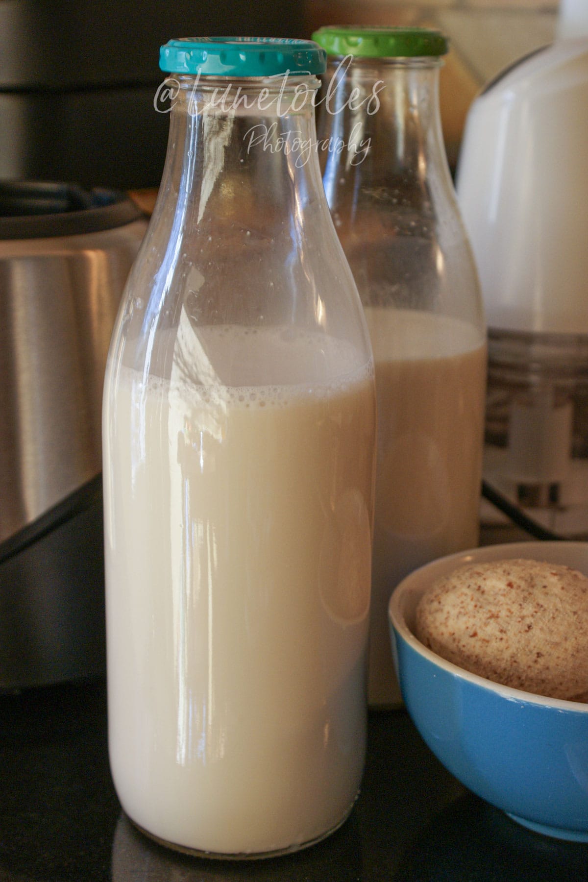 Bouteilles en verre remplies de lait d’amande maison, avec un bol d’okara d’amande après filtration.