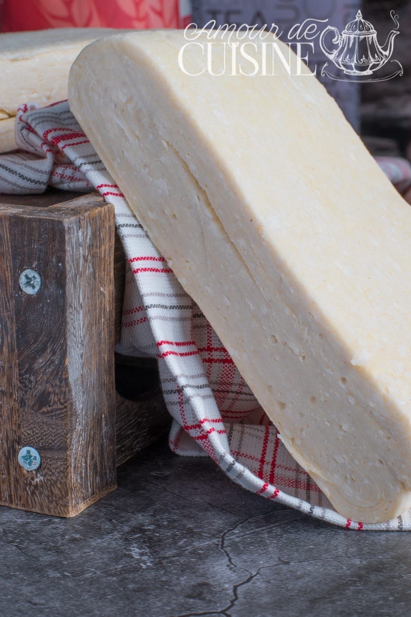 Homemade butter puff pastry dough shaped into a large log, resting on a red-check tea towel beside a wooden block on a grey countertop.