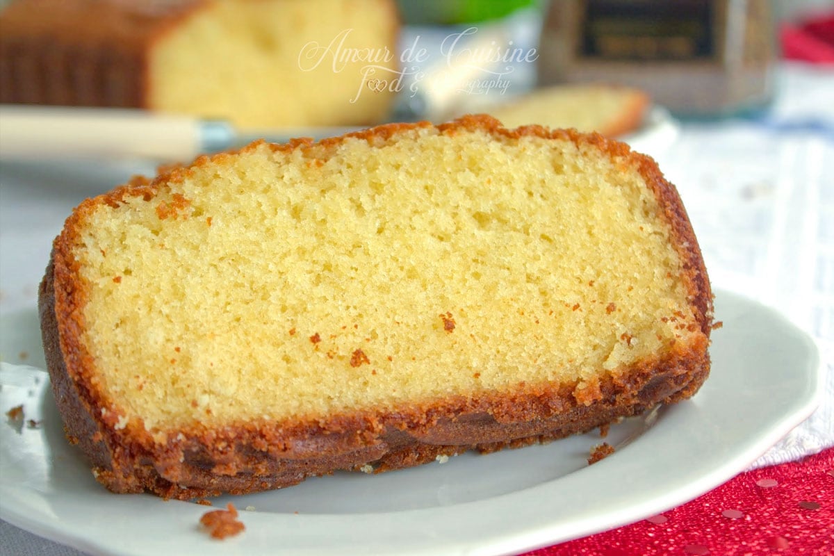 Tranche de quatre quart pur beurre à la mie fine et moelleuse, servie sur une assiette avec le gâteau flou en arrière-plan
