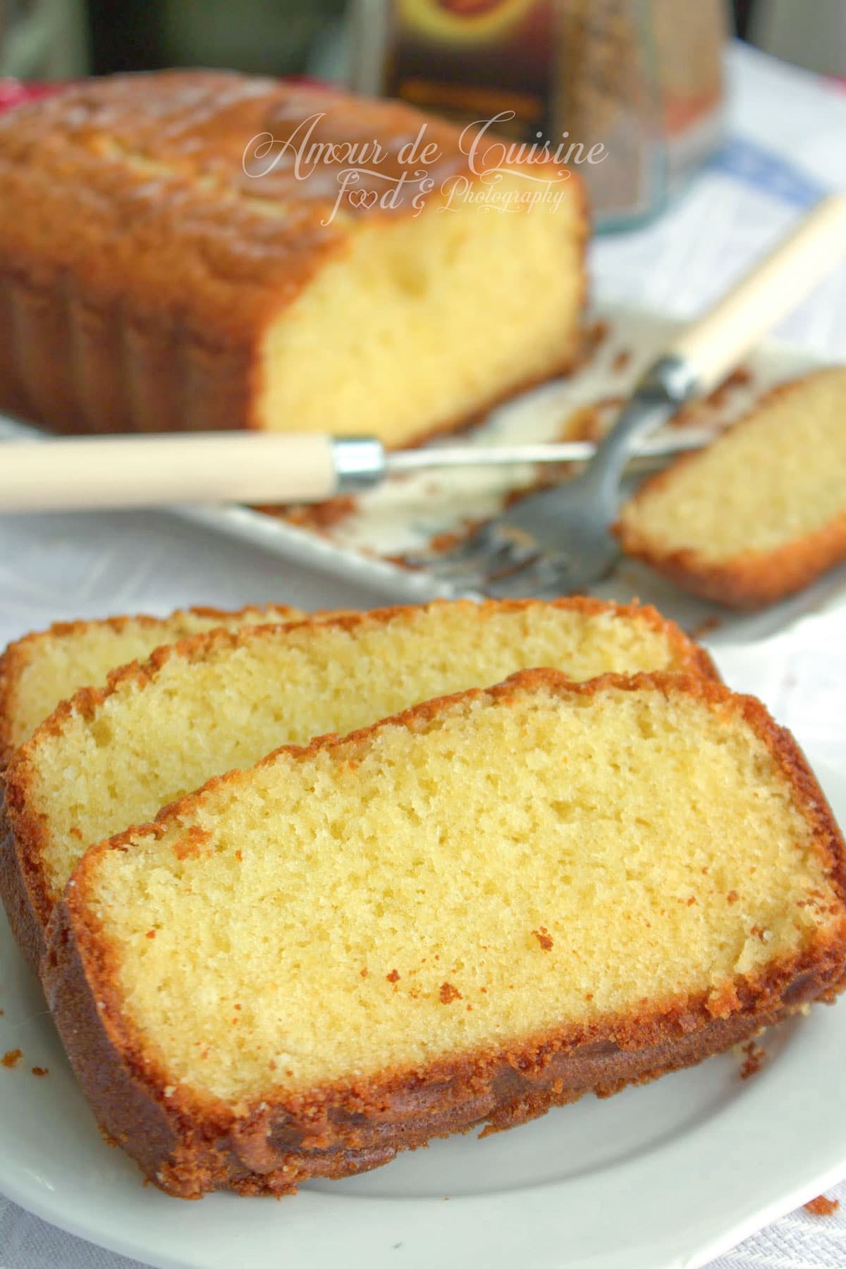 Quatre quart pur beurre coupé en tranches, à la mie moelleuse et dorée, présenté sur une assiette avec le cake entier en arrière-plan