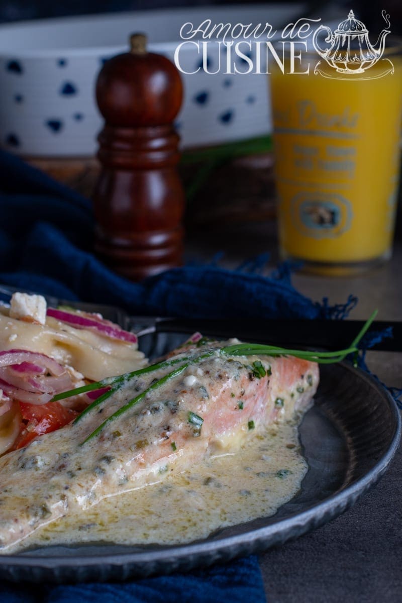 Oven-baked salmon fillet topped with a creamy lemon and chive sauce, served with pasta salad, tomatoes, and red onions – a refined, flavorful dish