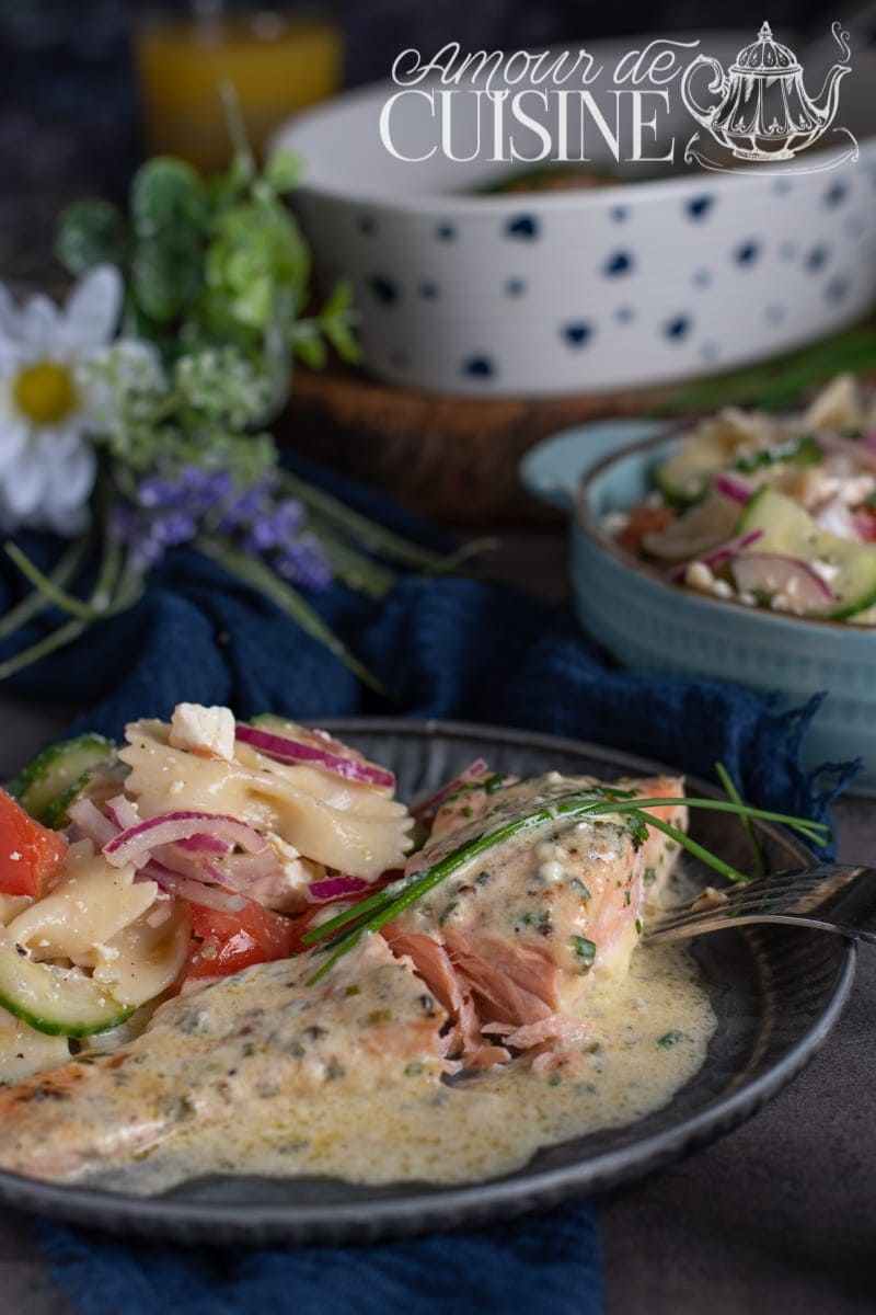 Oven-baked salmon fillet topped with creamy chive sauce, served with a pasta salad of tomatoes, cucumber, and red onion on an elegant plate.