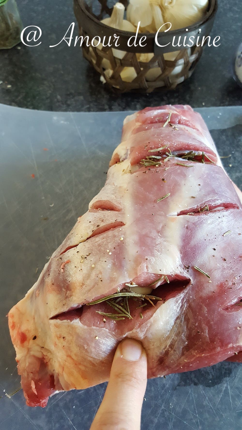 Gigot d’agneau cru entaillé, garni de gousses d’ail et de brins de romarin avant cuisson, prêt à être assaisonné