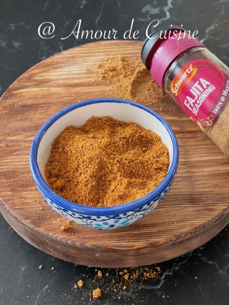 Bol de mélange d’épices fajitas sur une planche en bois, avec un flacon d’assaisonnement fajita renversé et des épices répandues autour.