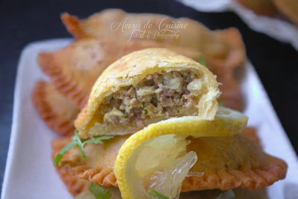 Close-up of a cut Algerian bourek laadjine : beef empanadas, showing the minced meat filling inside a golden crust, placed on a crispy pastry with lemon slices and a little parsley.