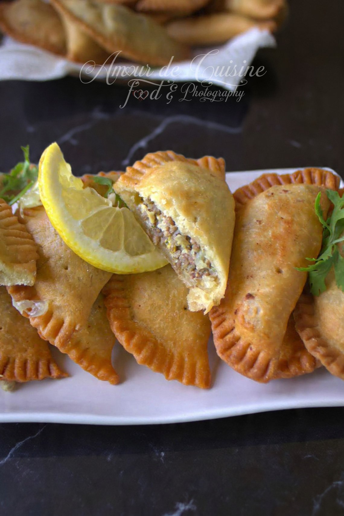 Golden, crispy Algerian pastels (bourek laadjine) filled with minced meat, served on a white platter with a lemon wedge and parsley, with one pastry cut open to show the filling.