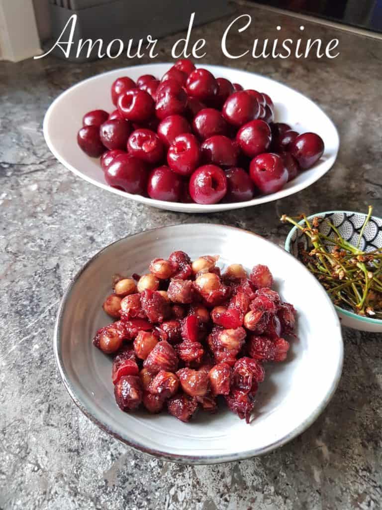Trois bols posés sur un plan de travail : un contenant des cerises rouges dénoyautées, un avec les noyaux, et un petit bol avec les queues de cerises