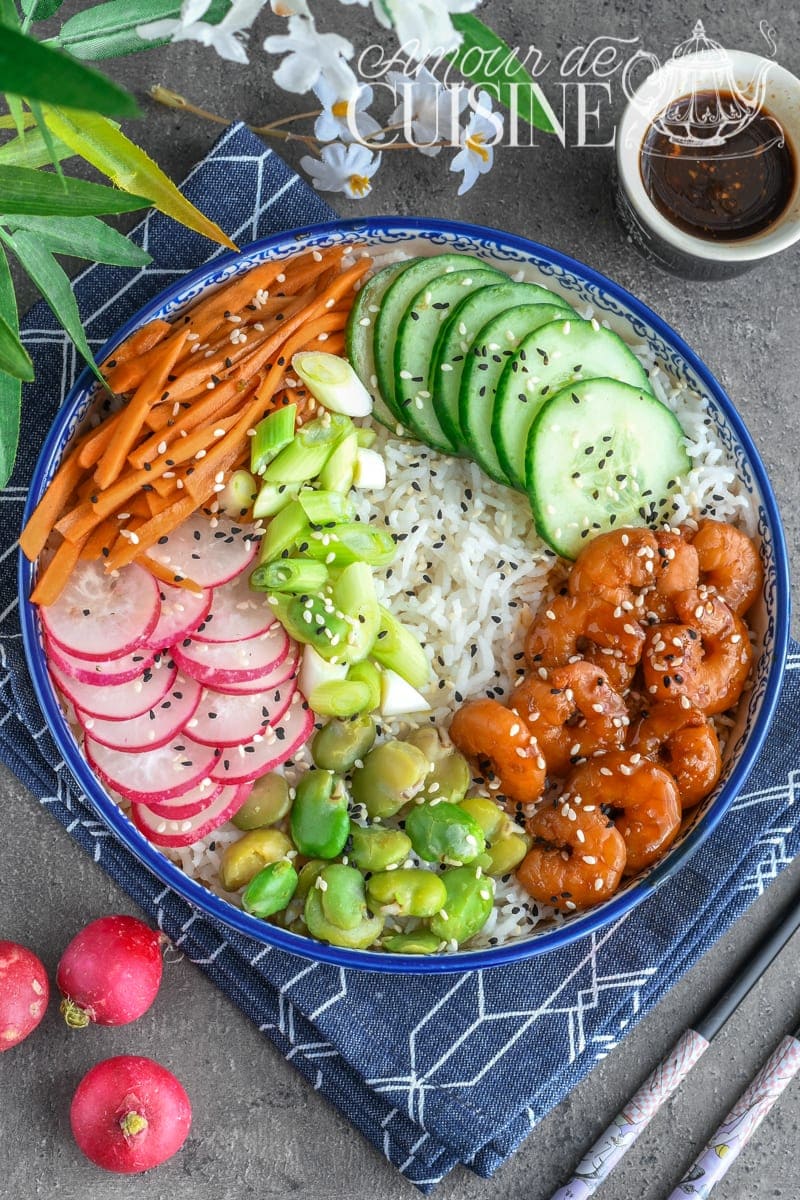 Poke bowl aux crevettes marinées au miel et à l’ail, servi avec riz blanc, concombre, radis, carottes, fèves et oignons nouveaux, garni de graines de sésame – recette saine et colorée facile à préparer.
