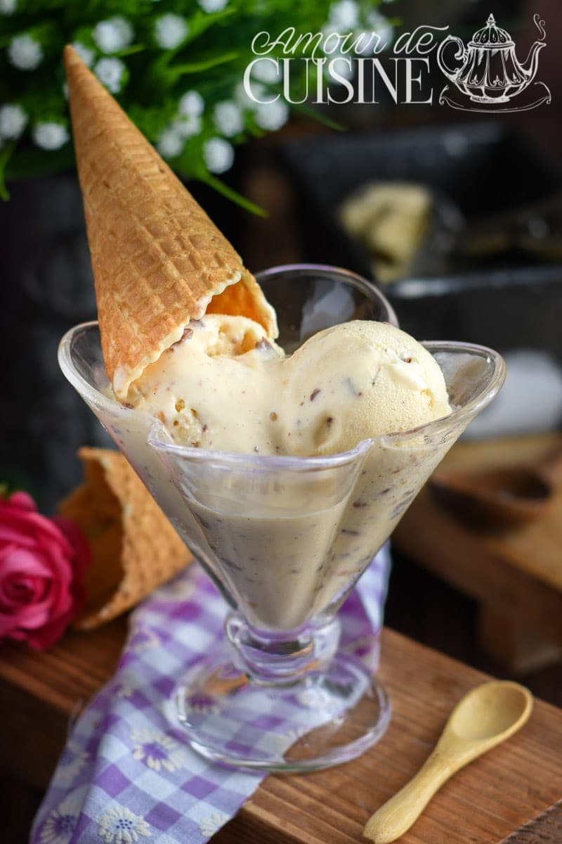 Crème glacée à la vanille maison servie dans une coupe en verre, garnie d’un cône croustillant, avec éclats de chocolat, sur fond rustique et nappe à carreaux violets