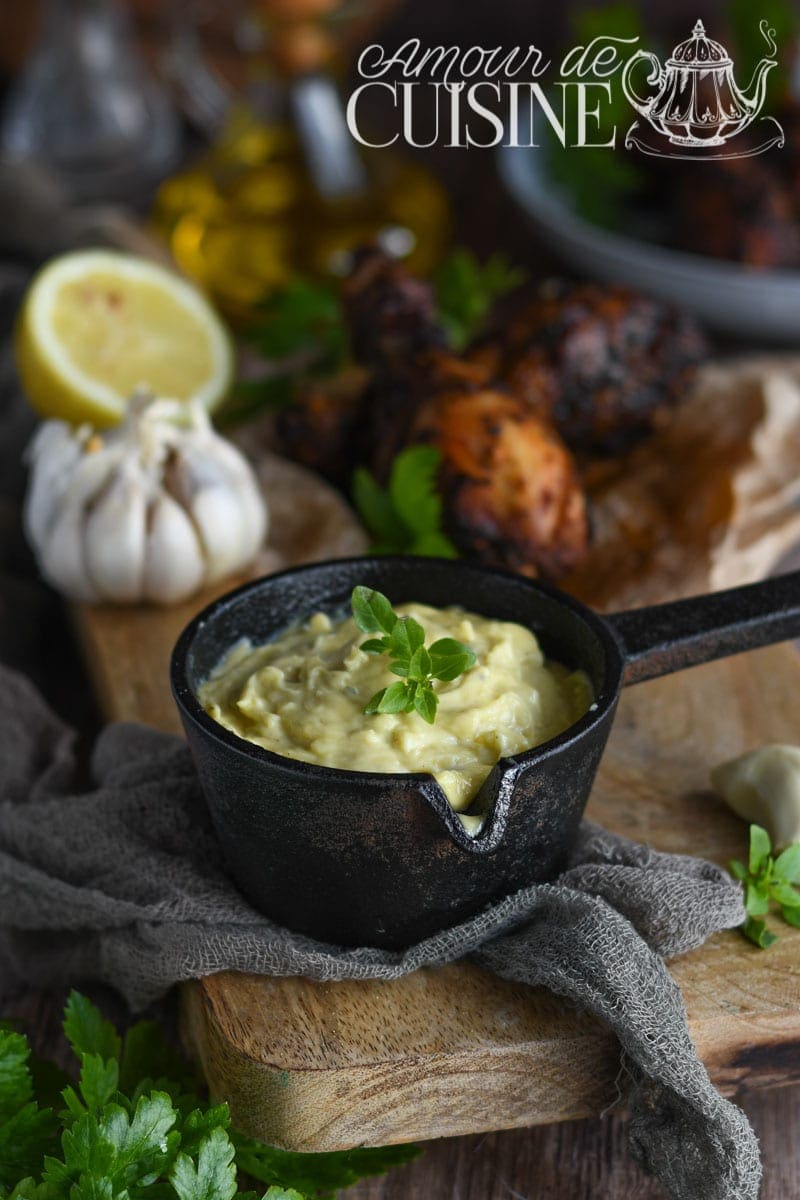 Sauce aïoli provençal maison dans une petite casserole en fonte, avec ail, citron et herbes fraîches en arrière-plan