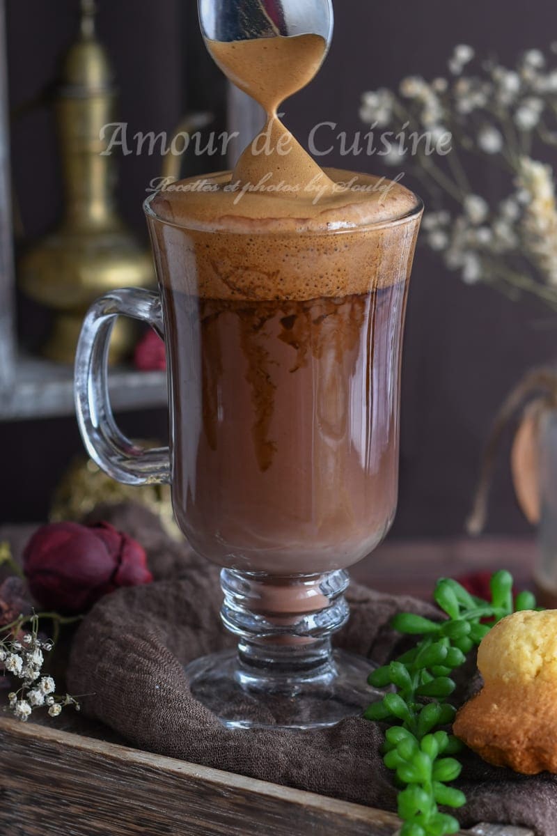 Glass of cocoa mocha coffee with chocolate swirls, topped with thick dalgona foam being spooned on top.