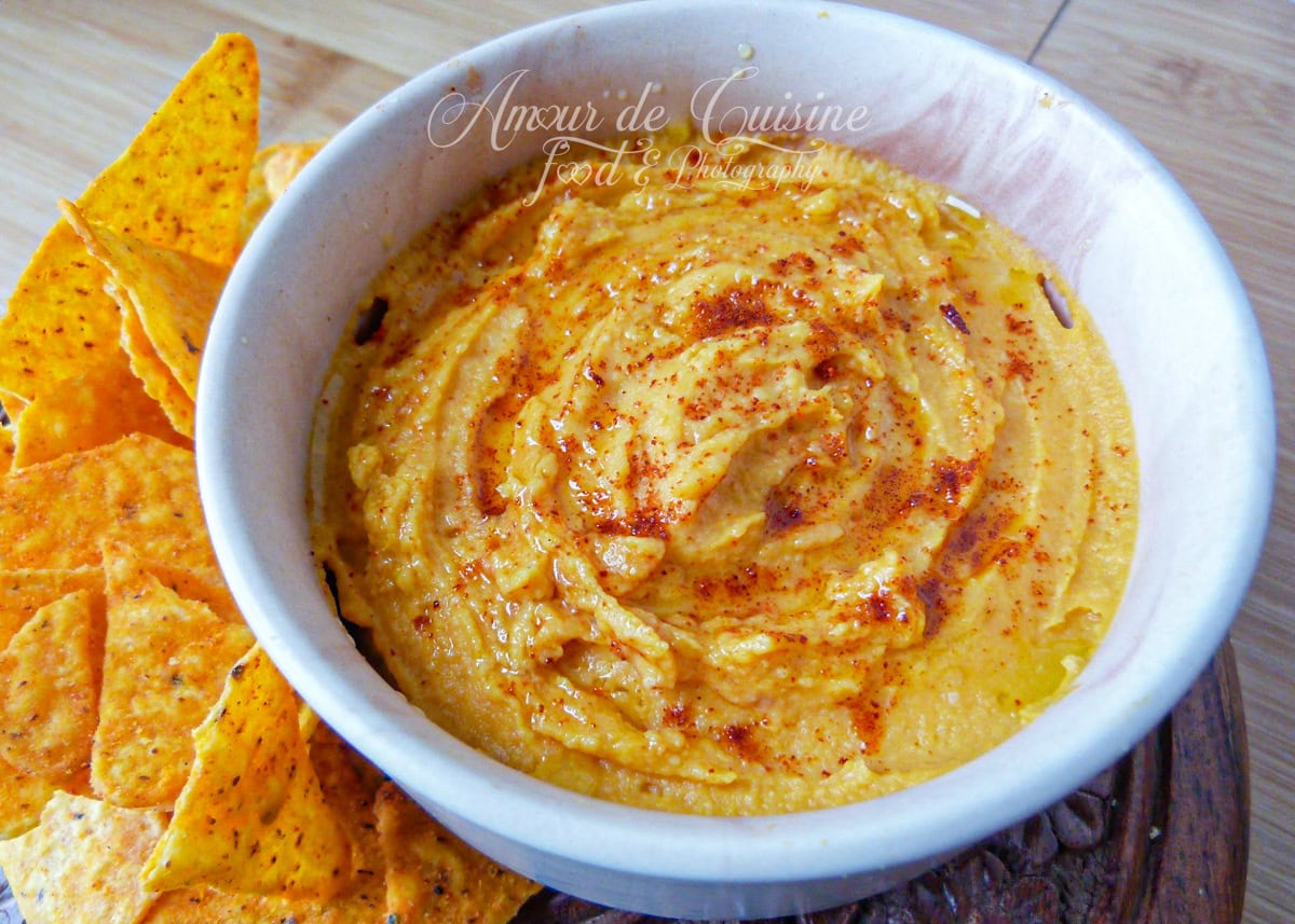 Bowl of creamy sweet potato hummus topped with a swirl of olive oil and sprinkled with paprika, served with crunchy tortilla chips on the side