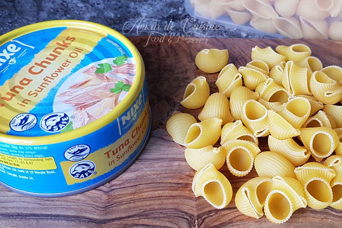 Boîte de thon à l’huile de tournesol et pâtes courtes crues disposées sur une planche en bois pour préparer un gratin de pâtes au thon.