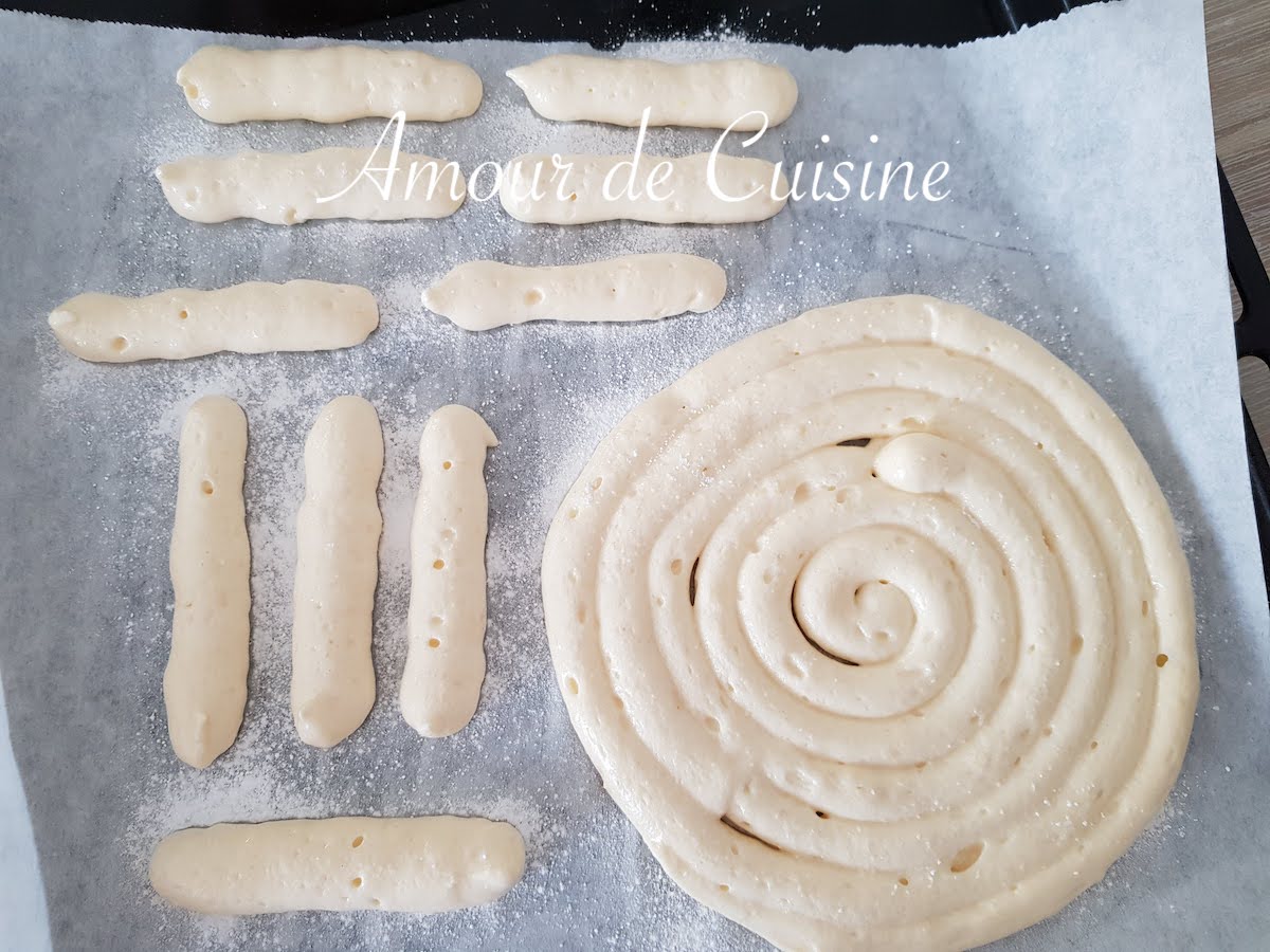 Ladyfinger batter piped onto a parchment-lined baking tray, forming both evenly spaced strips and a large spiral disc, ready to be baked.