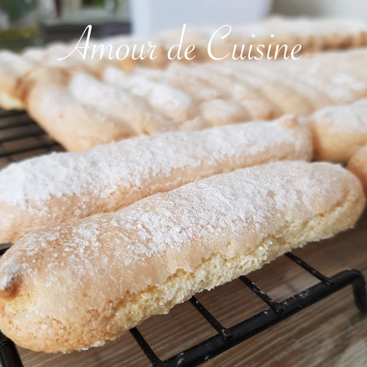 Freshly baked homemade ladyfingers, dusted with powdered sugar, arranged on a cooling rack to preserve their light and airy texture.