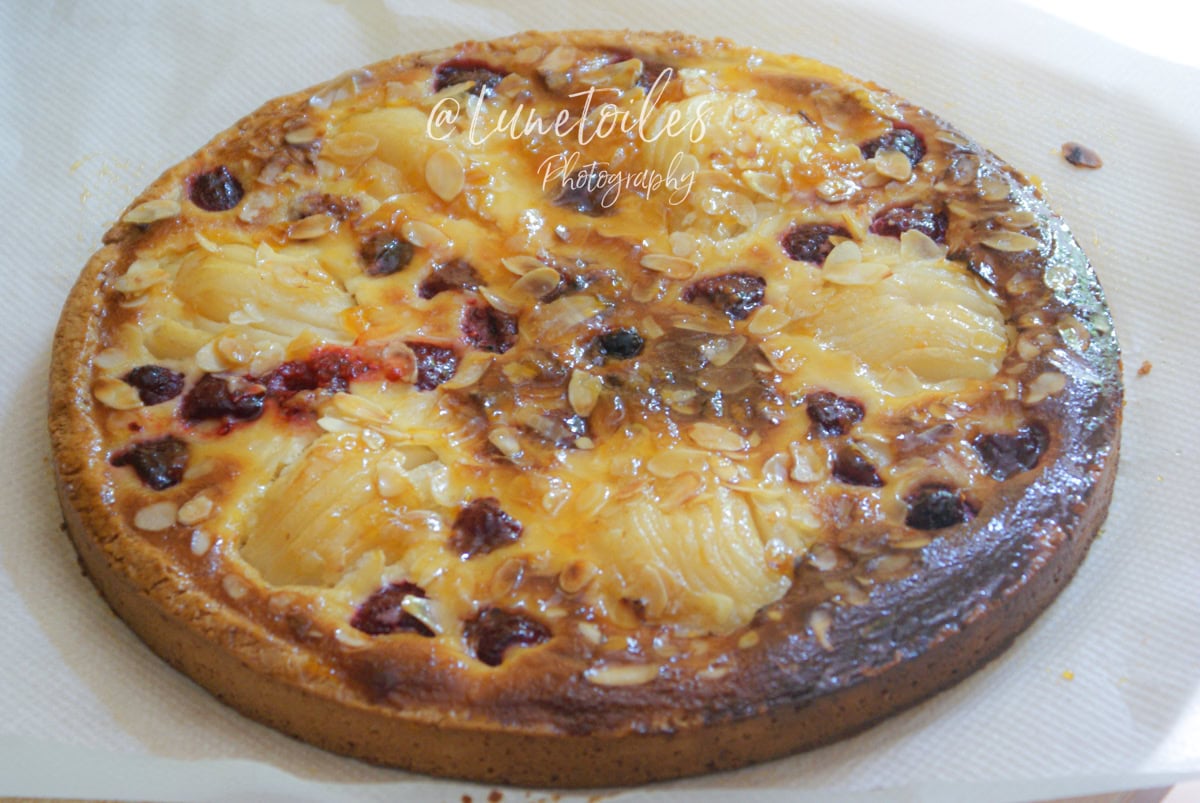 Tarte amandine entière, dorée au four, garnie de poires en lamelles, framboises et amandes effilées, posée sur une feuille de papier absorbant