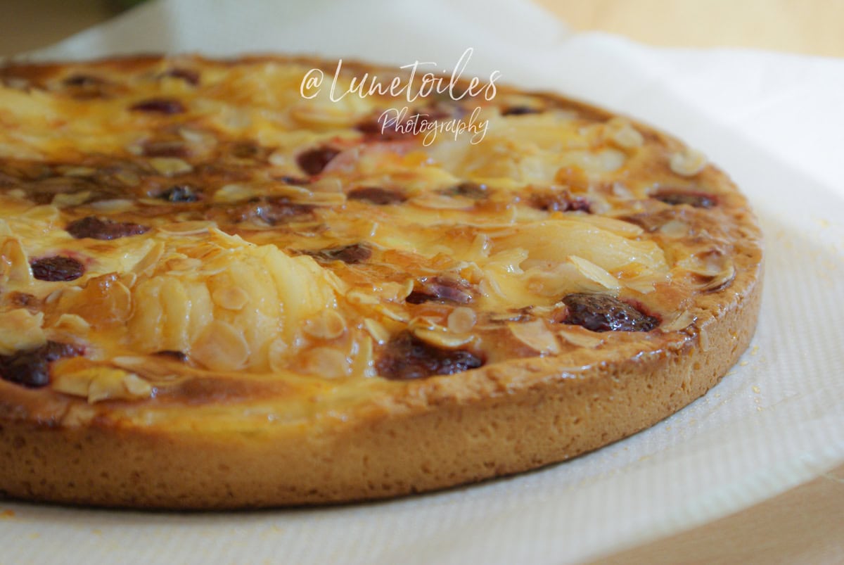 Tarte amandine aux poires et framboises entière, dorée et garnie d’amandes effilées, posée sur un plat recouvert de papier absorbant