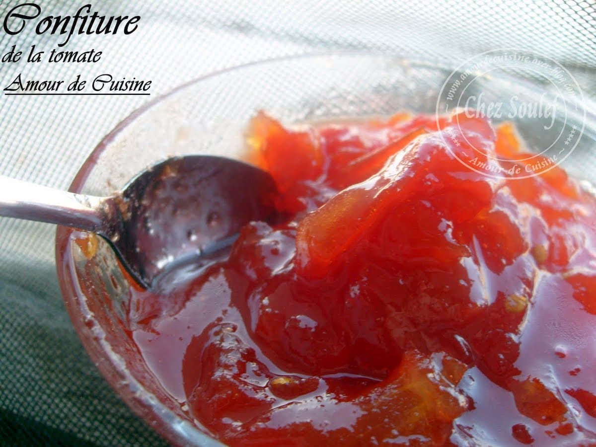 Gros plan sur une cuillère plongeant dans une confiture de tomate maison brillante et gourmande, avec des morceaux de tomates confites.