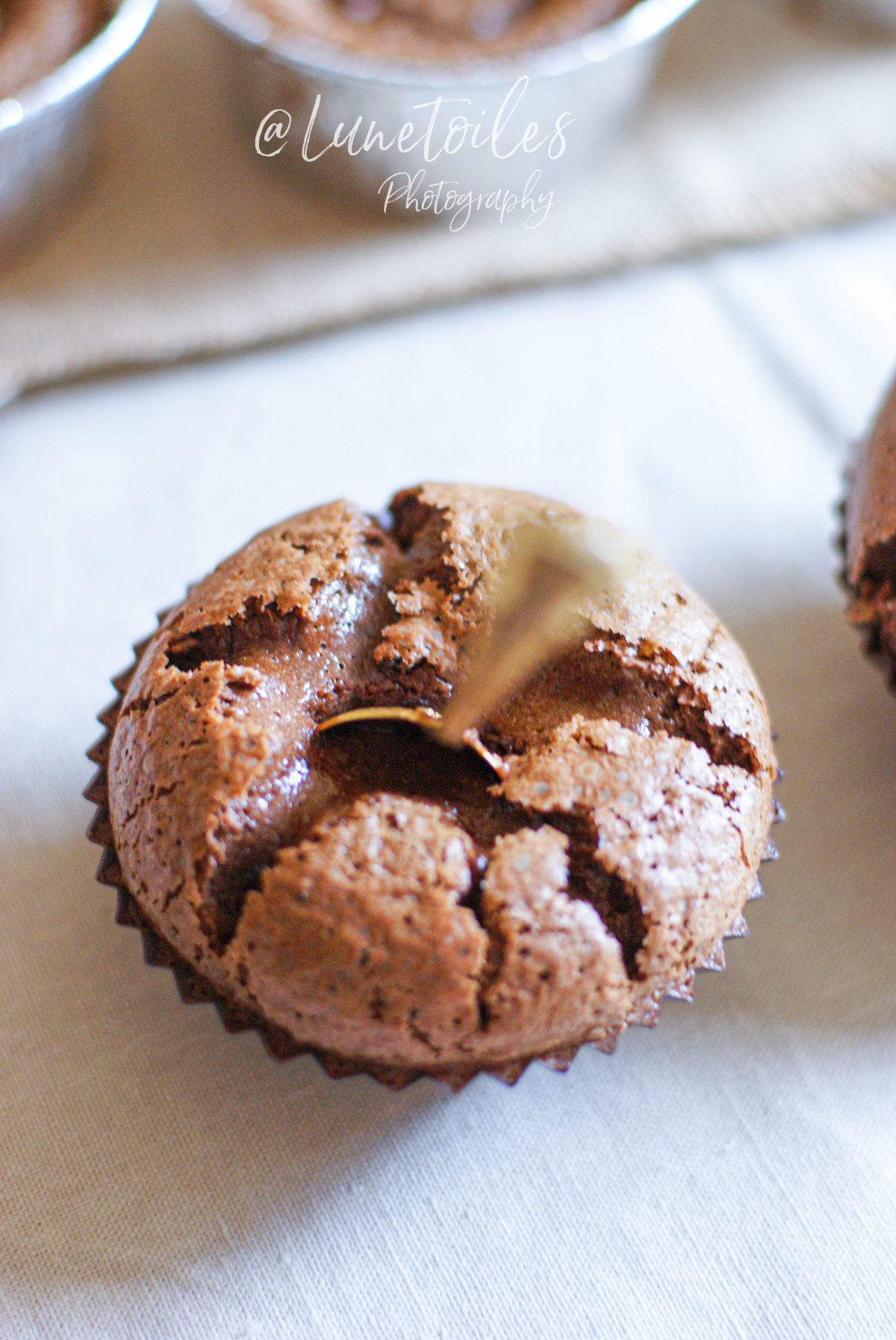 Fondant au chocolat individuel cuit dans une caissette en papier, au sommet craquelé laissant entrevoir un cœur coulant, avec une cuillère dorée plantée au centre