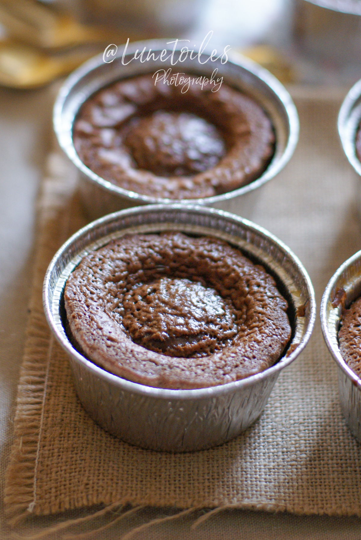 Petits moelleux au chocolat cuits dans des moules en aluminium, posés sur un morceau de toile de jute, avec leur croûte légèrement craquelée et gonflée au centre, prêts à être dégustés