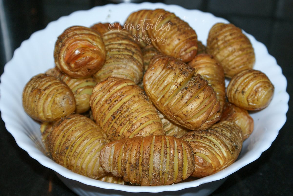 White bowl filled with small roasted hasselback potatoes, sliced into thin fan-like layers, golden and seasoned with herbs and spices.